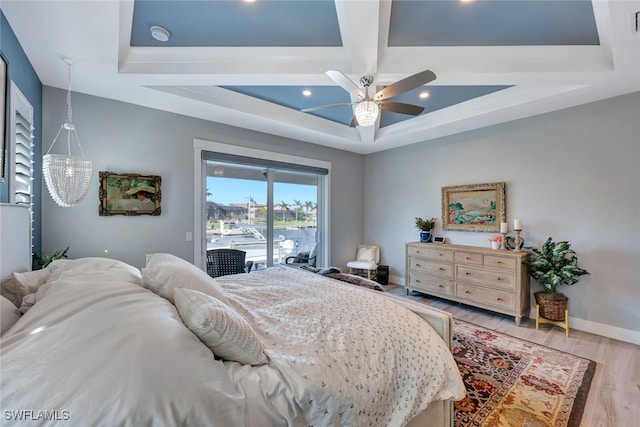 bedroom featuring access to outside, a raised ceiling, wood-type flooring, and ceiling fan with notable chandelier