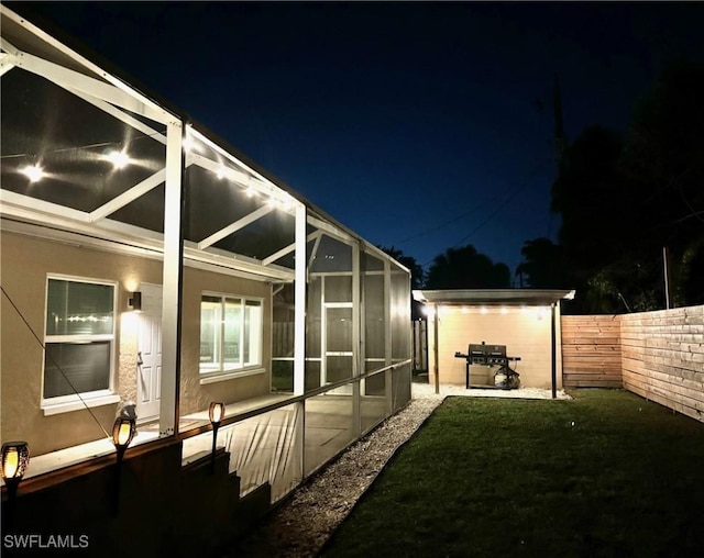 yard at twilight featuring glass enclosure and a patio area