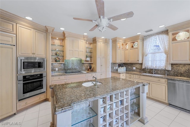 kitchen with built in appliances, a center island with sink, sink, light stone counters, and decorative backsplash