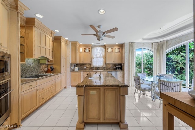 kitchen with tasteful backsplash, a kitchen island with sink, appliances with stainless steel finishes, light brown cabinetry, and dark stone countertops