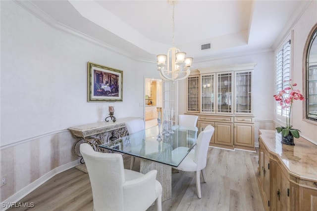 dining area with ornamental molding, light wood-type flooring, a chandelier, and a tray ceiling