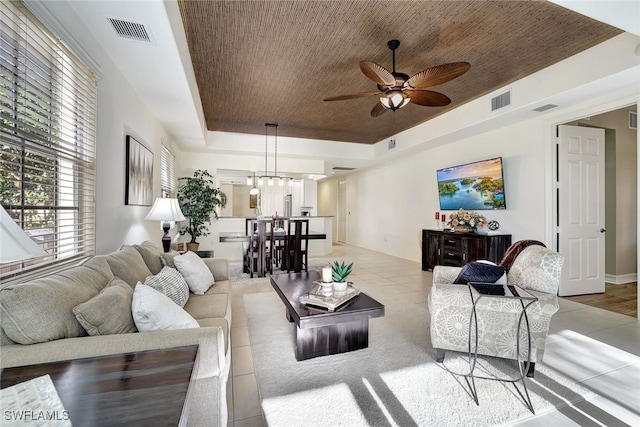 living room featuring wooden ceiling, ceiling fan with notable chandelier, and a tray ceiling