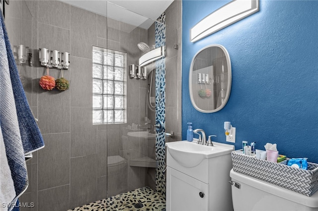 bathroom with a tile shower, vanity, and toilet