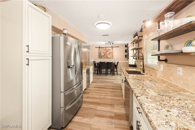 kitchen featuring sink, white cabinetry, appliances with stainless steel finishes, light stone counters, and light hardwood / wood-style floors