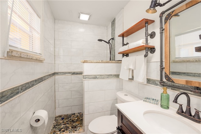 bathroom with toilet, vanity, a tile shower, and tile walls