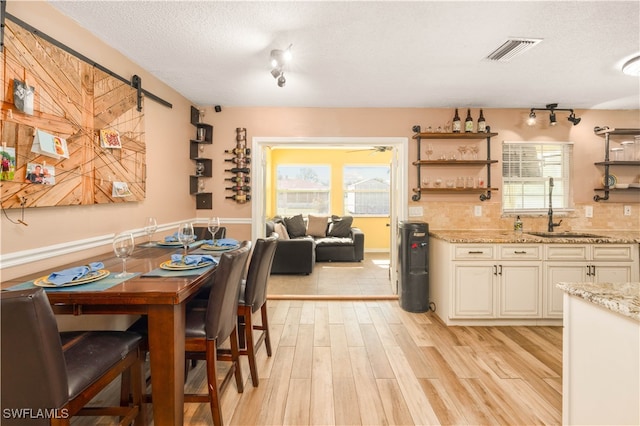 dining space with sink, a barn door, a textured ceiling, rail lighting, and light hardwood / wood-style flooring