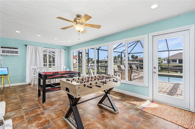 recreation room featuring a wall unit AC, ceiling fan, and plenty of natural light