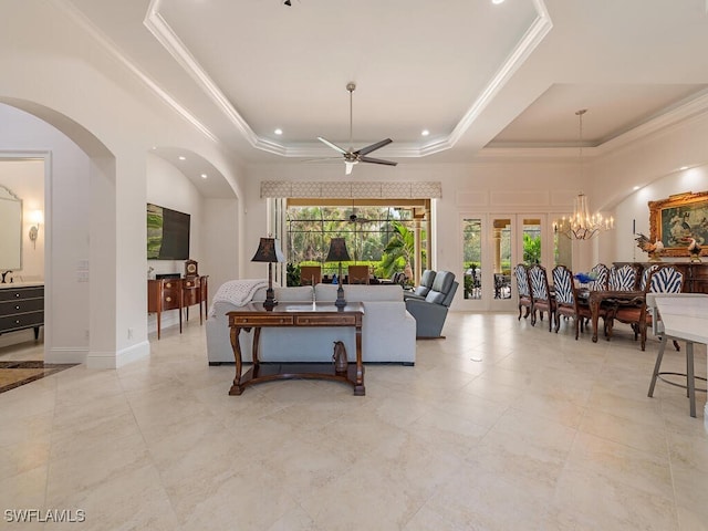 living room with crown molding, a towering ceiling, a tray ceiling, ceiling fan with notable chandelier, and french doors