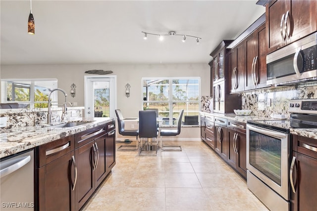 kitchen with stainless steel appliances, sink, light stone countertops, dark brown cabinets, and decorative backsplash