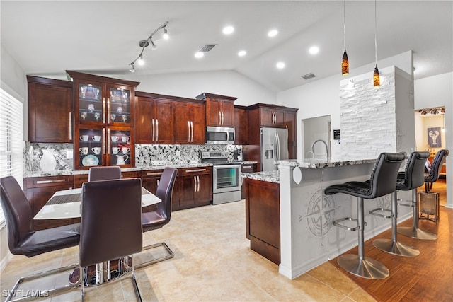 kitchen featuring light stone counters, vaulted ceiling, hanging light fixtures, tasteful backsplash, and appliances with stainless steel finishes