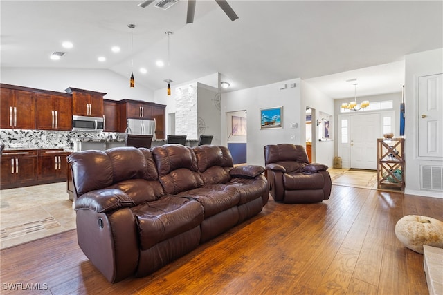 living room featuring dark wood-type flooring, ceiling fan with notable chandelier, and vaulted ceiling