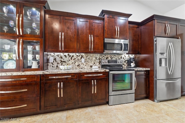 kitchen featuring stainless steel appliances, light stone countertops, light tile patterned floors, backsplash, and vaulted ceiling