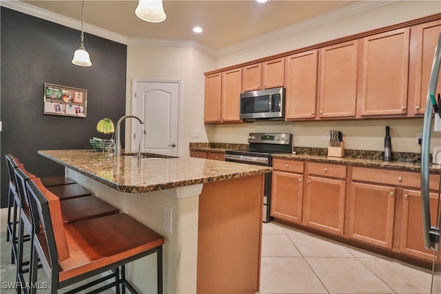 kitchen featuring a kitchen bar, stainless steel appliances, dark stone counters, crown molding, and a kitchen island with sink