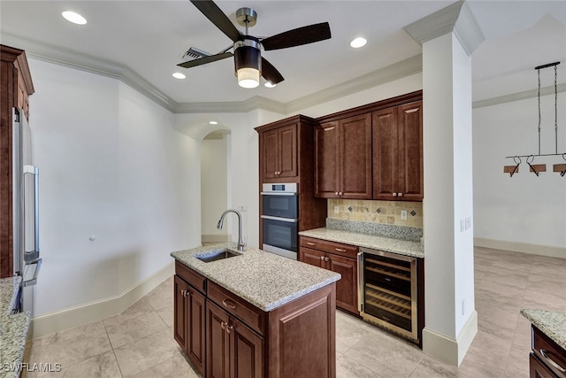 kitchen featuring crown molding, wine cooler, pendant lighting, sink, and a kitchen island with sink