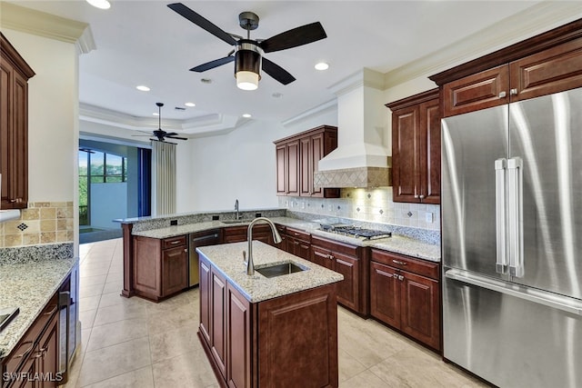 kitchen with stainless steel appliances, a center island with sink, ornamental molding, tasteful backsplash, and premium range hood