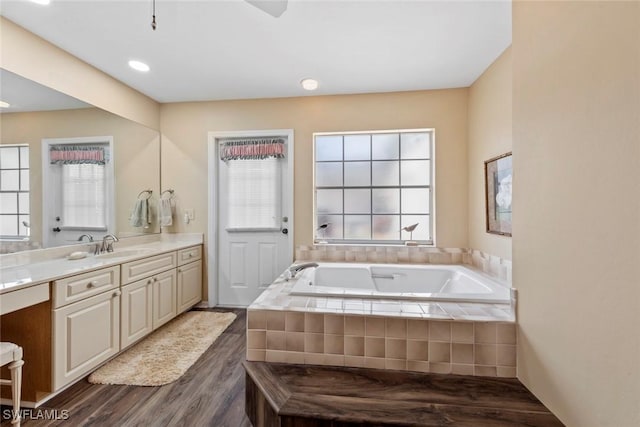 bathroom featuring wood-type flooring, tiled bath, and vanity