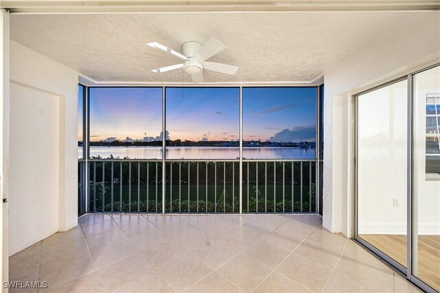 unfurnished sunroom with ceiling fan and a water view