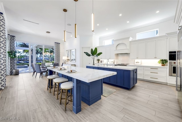 kitchen with a kitchen bar, custom exhaust hood, blue cabinets, a spacious island, and pendant lighting