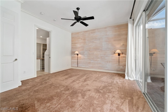 unfurnished bedroom featuring connected bathroom, wood walls, carpet, and ceiling fan