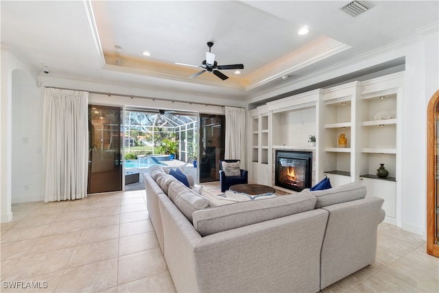 tiled living room featuring built in features, ceiling fan, crown molding, and a tray ceiling