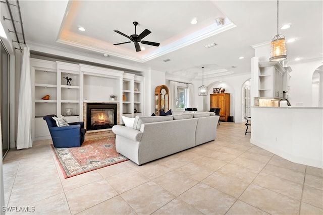 living room featuring built in shelves, a tray ceiling, ceiling fan, and crown molding