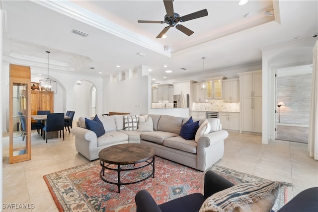 living room featuring light tile patterned flooring, ceiling fan with notable chandelier, crown molding, and a tray ceiling