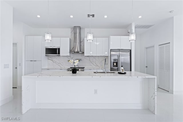 kitchen with appliances with stainless steel finishes, white cabinetry, wall chimney range hood, and pendant lighting