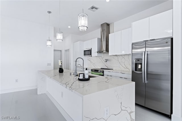 kitchen featuring wall chimney exhaust hood, appliances with stainless steel finishes, white cabinetry, and an island with sink