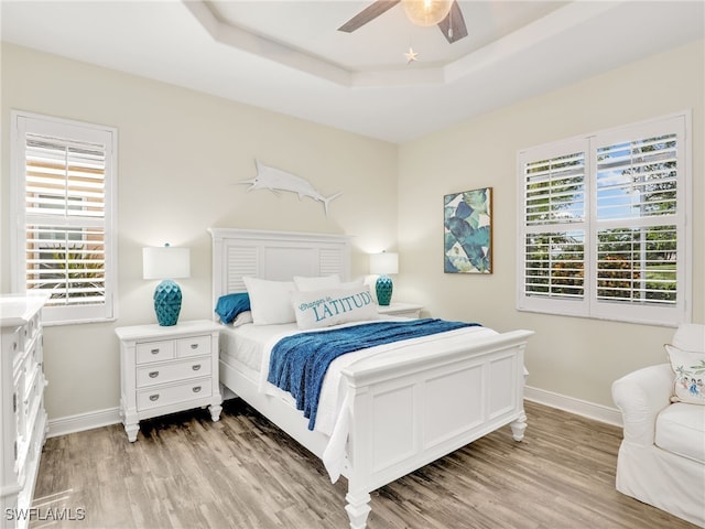 bedroom with a raised ceiling, ceiling fan, and light wood-type flooring