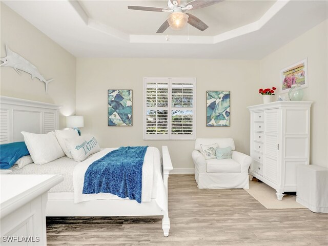 bedroom with a raised ceiling, ceiling fan, and light hardwood / wood-style flooring