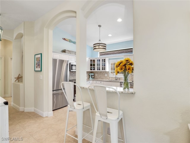 kitchen featuring light stone countertops, appliances with stainless steel finishes, tasteful backsplash, white cabinets, and hanging light fixtures