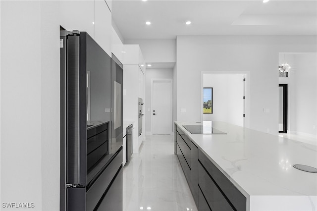 kitchen with light stone countertops, a large island, white cabinetry, and black appliances