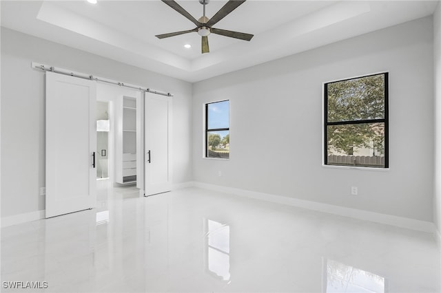 empty room featuring a healthy amount of sunlight, a barn door, ceiling fan, and a tray ceiling