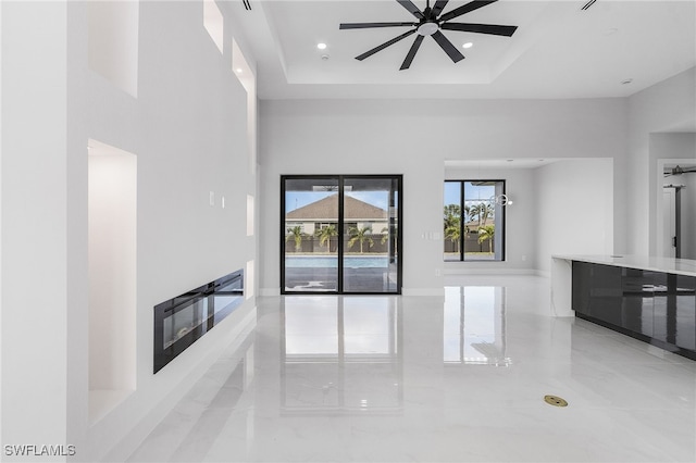 unfurnished living room featuring a high ceiling, ceiling fan, and a raised ceiling