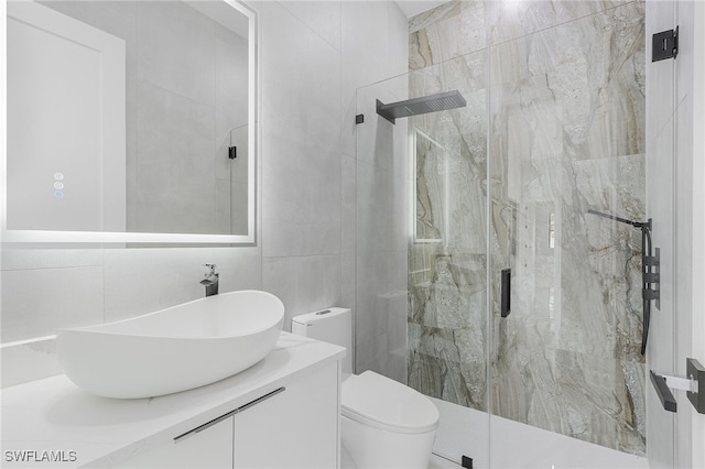 bathroom featuring a shower with shower door, vanity, toilet, and tile walls