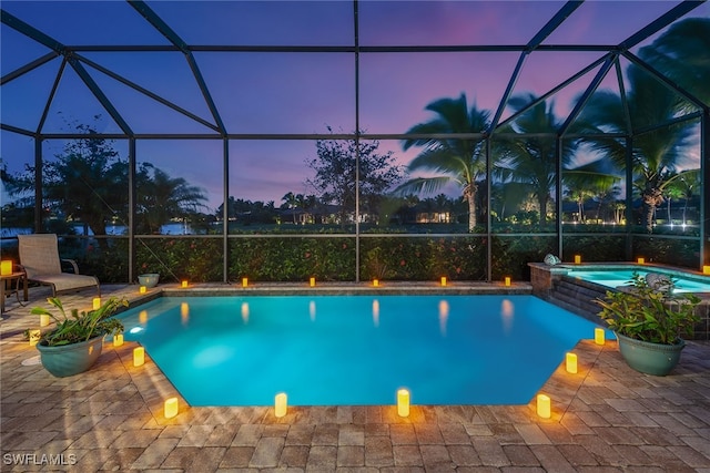 pool at dusk with glass enclosure, an in ground hot tub, and a patio area