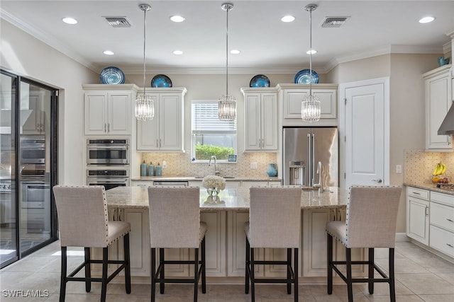 kitchen featuring decorative light fixtures, stainless steel appliances, light stone counters, and a kitchen island with sink