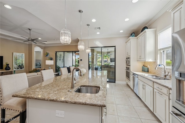 kitchen featuring a center island with sink, appliances with stainless steel finishes, decorative light fixtures, sink, and a kitchen breakfast bar