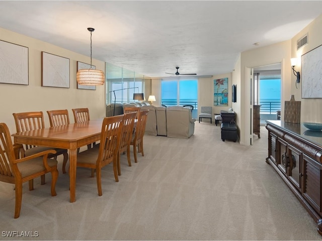 carpeted dining area with a wealth of natural light, a water view, and ceiling fan