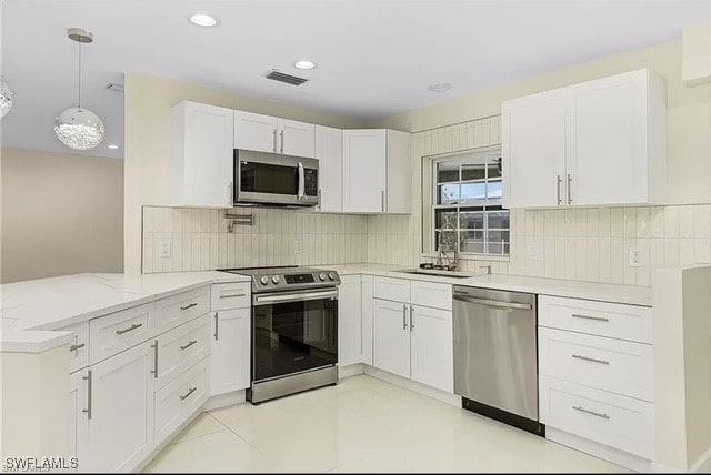 kitchen featuring light stone counters, backsplash, white cabinetry, appliances with stainless steel finishes, and hanging light fixtures