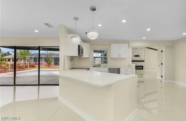 kitchen with stainless steel appliances, light stone counters, white cabinets, decorative backsplash, and decorative light fixtures