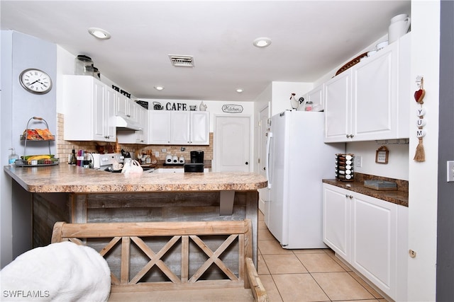 kitchen with kitchen peninsula, light tile patterned floors, white cabinetry, stove, and white refrigerator