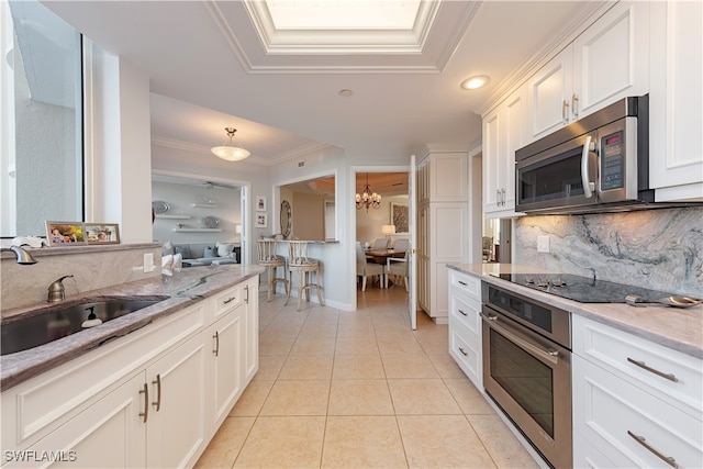 kitchen with stainless steel appliances, white cabinetry, backsplash, sink, and a chandelier