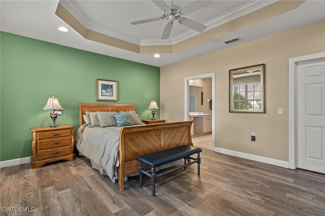 bedroom with ornamental molding, dark wood-type flooring, ensuite bathroom, and a tray ceiling