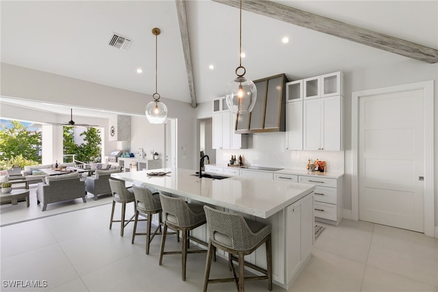 kitchen featuring pendant lighting, a kitchen island with sink, sink, white cabinetry, and a breakfast bar area