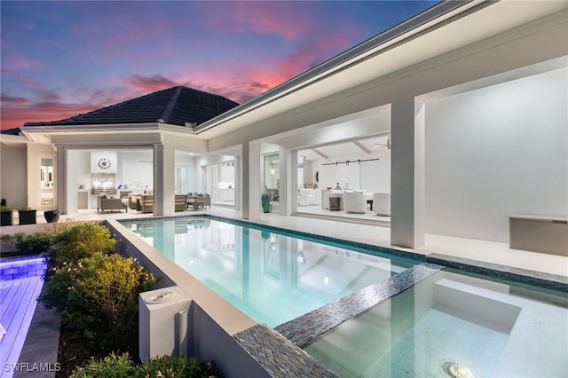 pool at dusk with a patio area, an outdoor hangout area, and an in ground hot tub