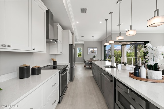 kitchen with sink, hanging light fixtures, stainless steel appliances, wall chimney exhaust hood, and white cabinets