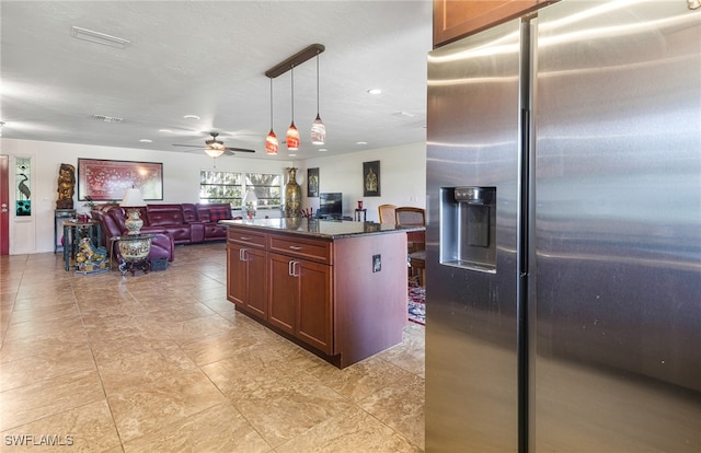 kitchen featuring a center island with sink, dark stone counters, decorative light fixtures, stainless steel fridge with ice dispenser, and ceiling fan