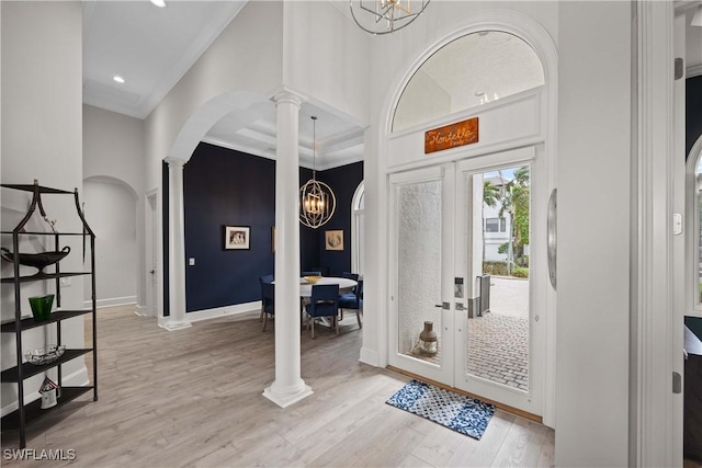 entryway with ornamental molding, light wood-type flooring, a towering ceiling, and an inviting chandelier