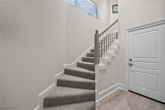 stairs featuring a high ceiling, baseboards, and wood finished floors